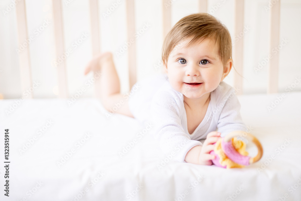 a small child close-up on a white cotton bed at home with a pink rodent, the baby is teething a small child close-up on a white cotton bed at home with a pink rodent, the baby is teething
