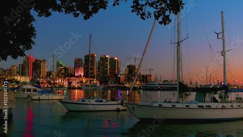 Marina with boats and illuminated city skyline at dusk in San Diego, California in 4k