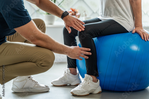 Physiotherapist helping senior woman with leg rehabilitation exercise on balance ball photo