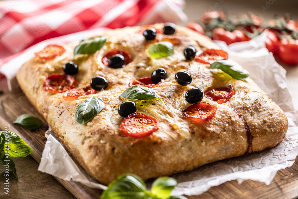 Focaccia - Italian Bread with tomatoes basil leaves olives and olive oil on cutting board