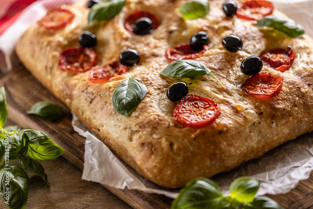 Focaccia - Italian Bread with tomatoes basil leaves olives and olive oil on cutting board