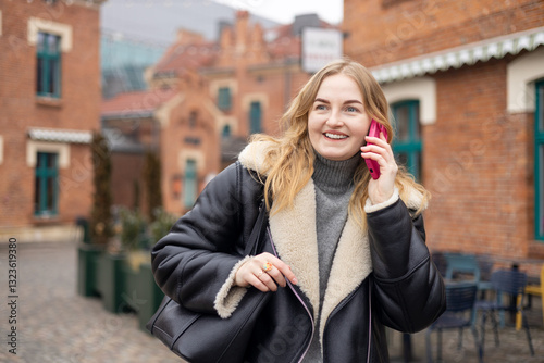 Happy 30s woman talking phone and look happy outdoors. Urban lifestyle concept. Winter time. Beautiful blonde curly woman walking on the city street.