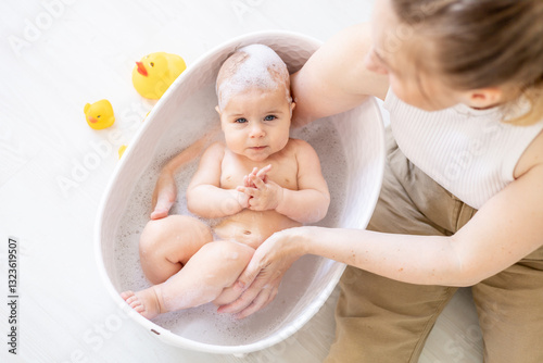 mom's hands bathe a small newborn baby in a bubble bath, washing the baby