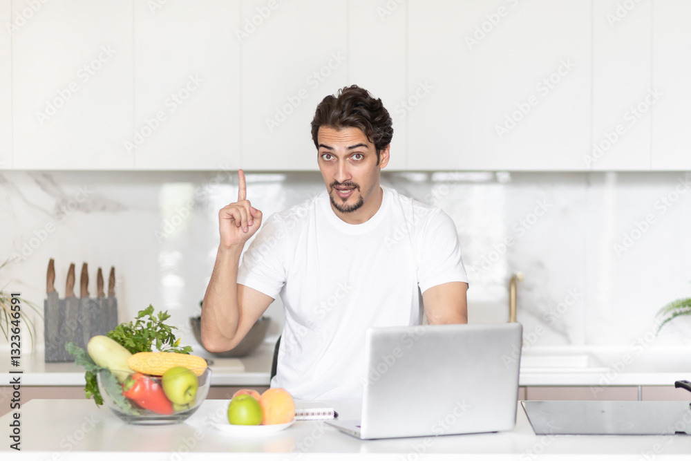 Young handsome and fit man sitting at the table in the kitchen and writing his diet plan in notebook. A lot of fruits and vegetables which on the table also included in his ration Young handsome and fit man sitting at the table in the kitchen and writing his diet plan in notebook. A lot of fruits and vegetables which on the table also included in his ration