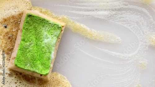 Soapy green sponge on a greasy surface with drifting fat, capturing thorough dishwashing action and focus on essential cleanliness