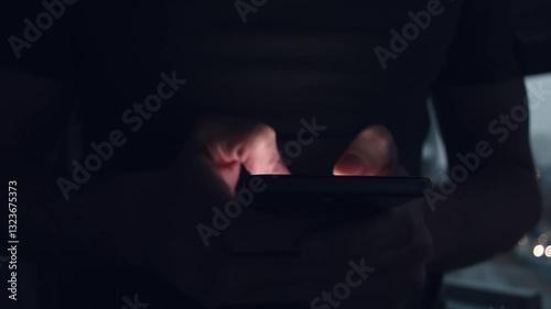 Close-up of man typing on smartphone in dim room, fingers illuminated by phone screen glow, night messaging concept in dark interior.