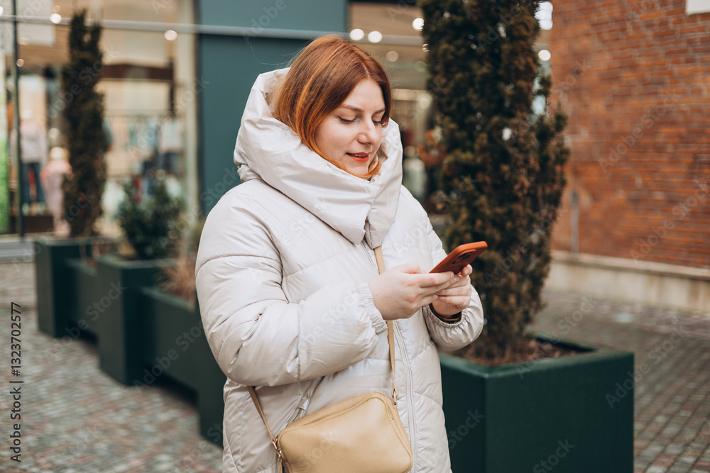 Young stylish 30s woman writes message on smartphone walking on city street. Urban lifestyle concept. Autumn time. Charming female wearing stylish outfit chatting online. High quality photo.
