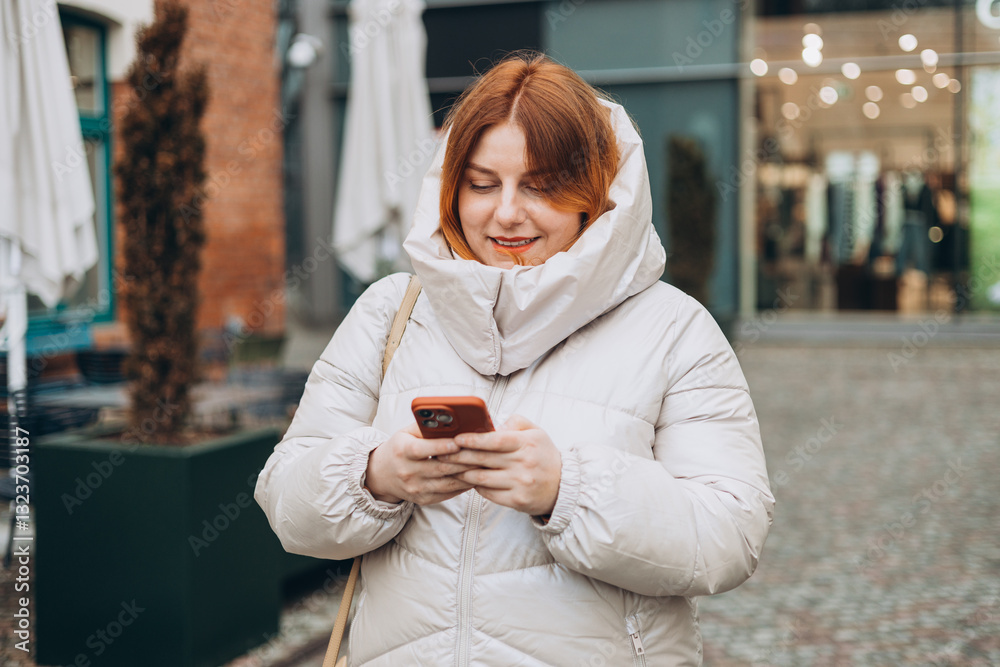 Young stylish 30s woman writes message on smartphone walking on city street. Urban lifestyle concept. Autumn time. Charming female wearing stylish outfit chatting online. High quality photo.
