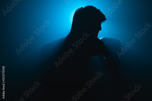 Silhouette of an Asian male boxer in fighting stance, lit by dramatic blue backlight and surrounded by haze, creating a moody and intense athletic atmosphere in studio
