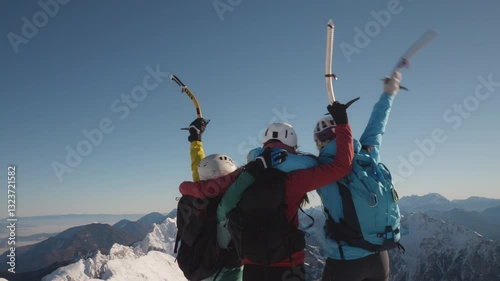 Three people celebrate reaching the summit of a snowy mountain, holding ski poles and wearing backpacks.