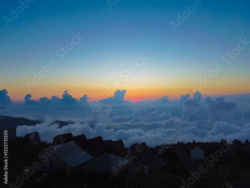 Obraz na płótnie Sun sets over the mountain village, illuminating the sea of clouds below and creating a striking contrast between the dark silhouettes of the village and the bright sky w salonie