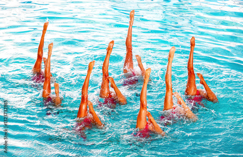 Swimmers performing synchronized routine in clear blue pool during sunny day