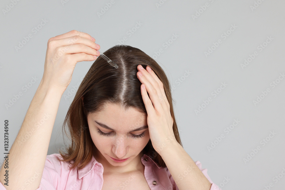 Hair loss problem. Girl applying serum onto hairline on grey background