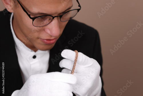 Appraiser evaluating luxury jewelry on beige background, closeup
