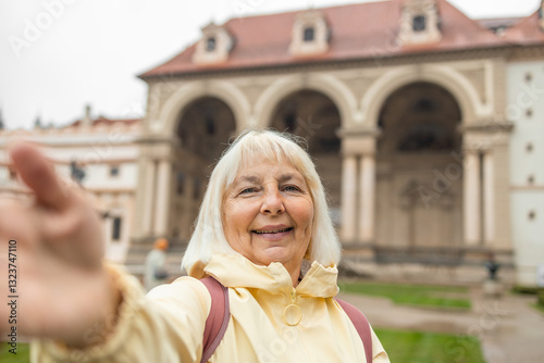 Happy 60s blonde elderly woman takes a selfie in Prague gardens at summer holiday in Europe. View of the Waldstein park in Prague-a famous tourist attraction. Prague, Czech Republic. High quality