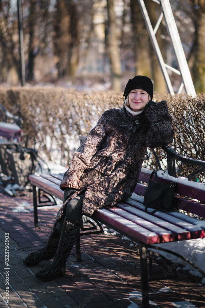A woman in a karakul fur coat sits on a bench in a snowy park, surrounded by the quiet beauty of winter.