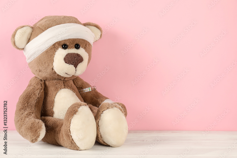 Fototapeta premium Teddy bear with bandages and thermometer on white wooden table against pink background, space for text