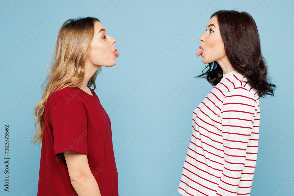 Side view young couple playful two friends women wear red casual clothes together look to each other show tongue isolated on pastel plain light blue cyan background studio portrait. Lifestyle concept. Side view young couple playful two friends women wear red casual clothes together look to each other show tongue isolated on pastel plain light blue cyan background studio portrait. Lifestyle concept.