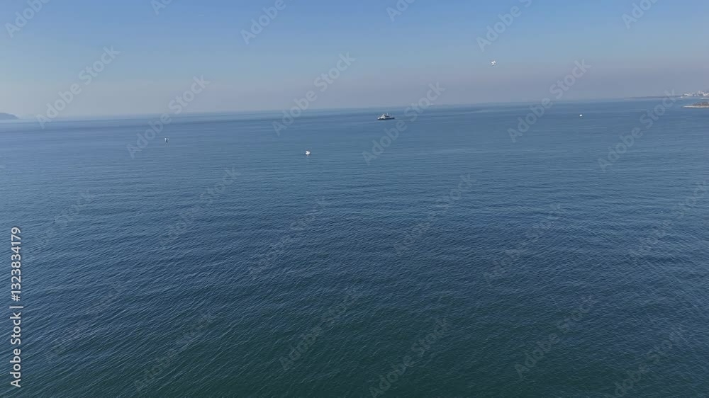 A breathtaking drone view of the sea on a sunny day, with birds soaring above the water. The waves reflect the sunlight, while the city’s coastline appears in the background, adding depth to the view. A breathtaking drone view of the sea on a sunny day, with birds soaring above the water. The waves reflect the sunlight, while the city’s coastline appears in the background, adding depth to the view.