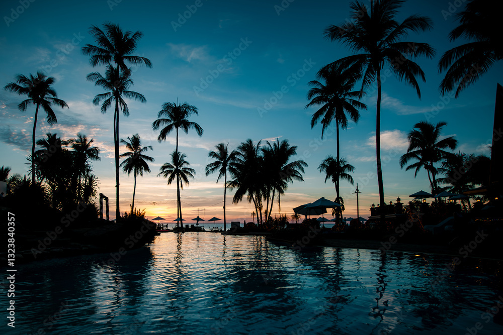 Twilight on a tropical beach with silhouettes of palm trees and their reflections shimmering in the calm water.