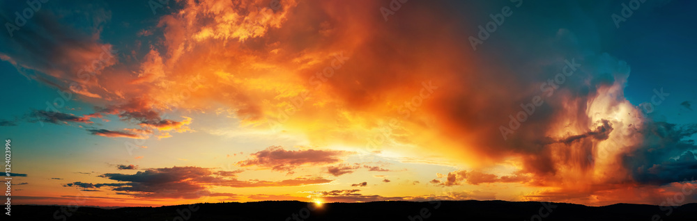 Obraz premium Dramatic storm clouds lit in vivid orange and yellow colors at sunset. A panoramic weather shot 