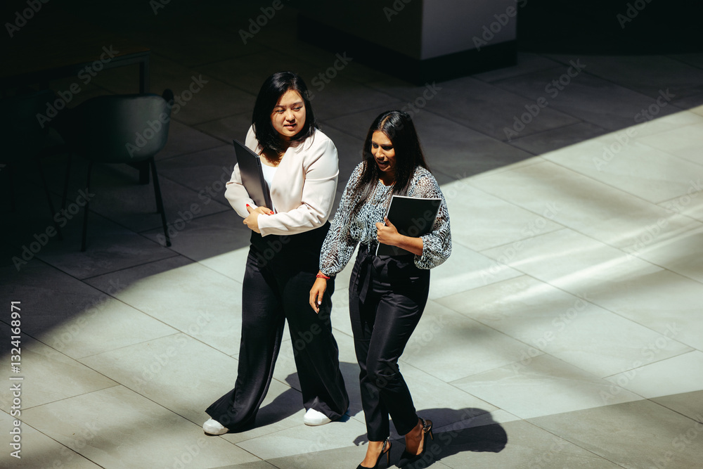 © Jacob Lund - Female colleagues walking together in modern office setting