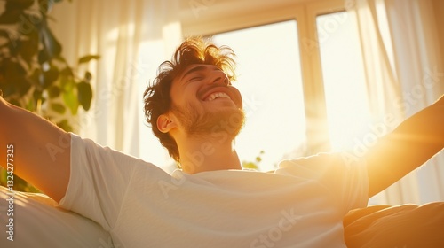 A young man waking up in bed, stretching his arms with a relaxed smile as warm morning sunlight streams through the window.