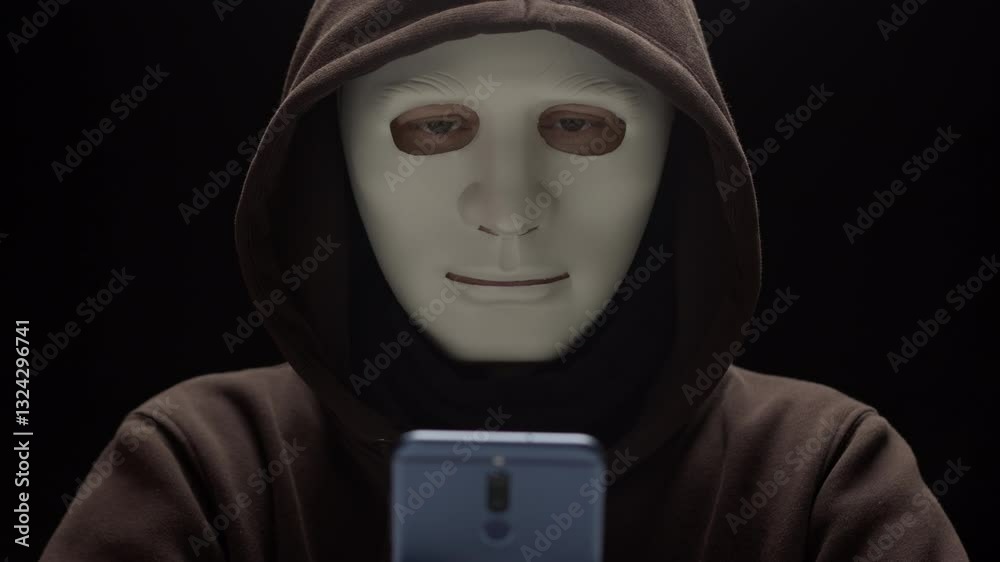 Masked criminal uses phone to commit fraud. Concept of hacking and cybersecurity via smartphone. Masked criminal uses phone to commit fraud. Concept of hacking and cybersecurity via smartphone.