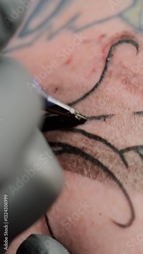 In this vertical 4K 60 fps macro video, a tattoo artist applies black ink to his skin. The camera focuses on the precise lines being drawn, with a towel wipe during the tattooing process.