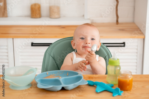 a baby boy eats baby puree in a high chair, a small child eats on his own with a spoon, baby food photo