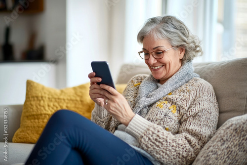 Happy middle-aged elderly woman uses smartphone while sitting on the sofa in her home