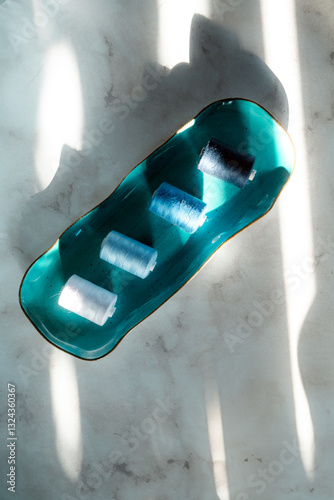 Colorful (shades of blue) sewing threads on a blue oblong plate in streak of light, top view