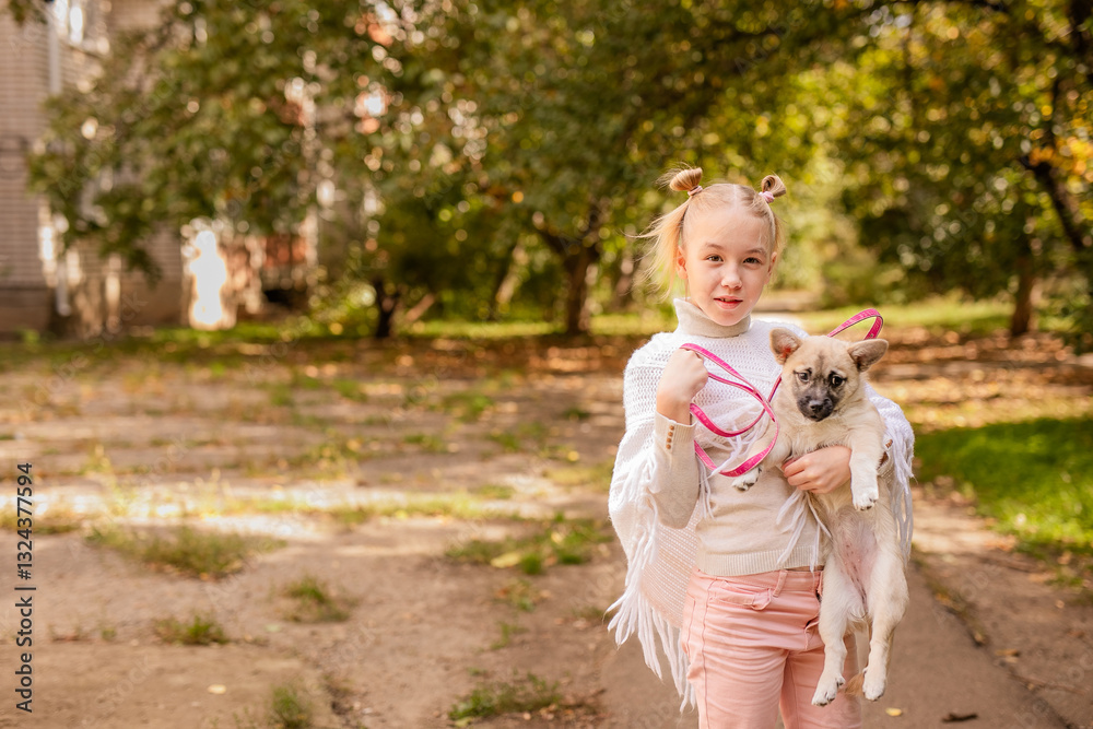 Obraz premium Blonde girl in a white poncho holding a small dog in a warm, sunny, old park