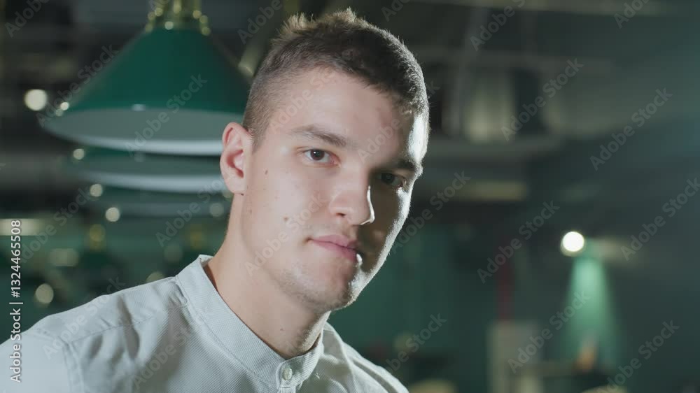 Close-up of man in white shirt with slight smile in dimly lit billiards hall. Overhead lights create soft reflections on his face. Green pool table and hanging lights add depth to modern ambiance Close-up of man in white shirt with slight smile in dimly lit billiards hall. Overhead lights create soft reflections on his face. Green pool table and hanging lights add depth to modern ambiance