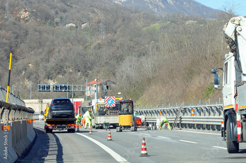 Reduced driving lane on the highway and industrial vehicles and a bulldozer during viaduct maintenance work and a tow truck carrying the broken down car photo