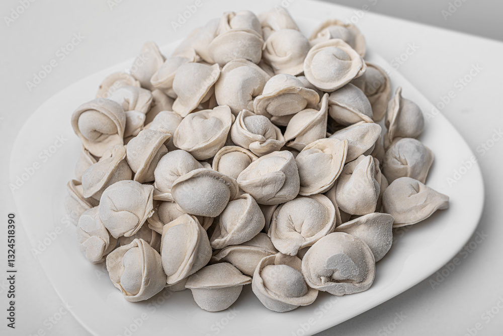 A plate full of raw, frozen pelmeni, traditional dumplings made of dough filled with meat, showcasing their distinct shape and texture.