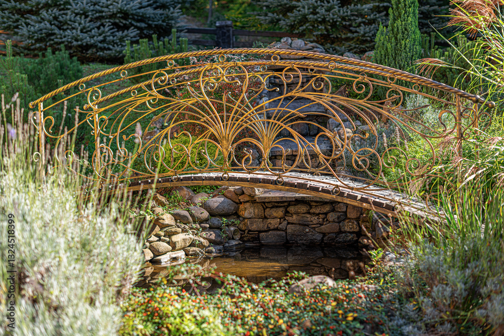 A beautifully crafted wrought iron bridge with intricate golden detailing spans a small garden stream, surrounded by lush greenery and bathed in warm sunlight.