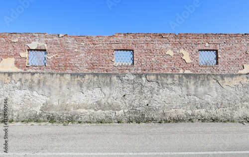 Grunge wall at the roadside. It is made of rough concrete in the lower side and bricks in the upper with remains of plaster. Street in front. Background for copy space