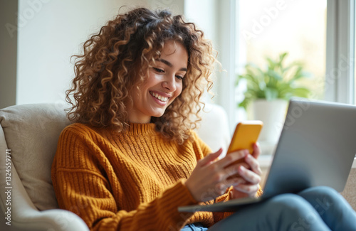 Smiling young adult pretty woman sits on chair using smartphone. Mobile cellphone tech for remote work or distance learning at home office. Happy female texts messages, checks email. photo