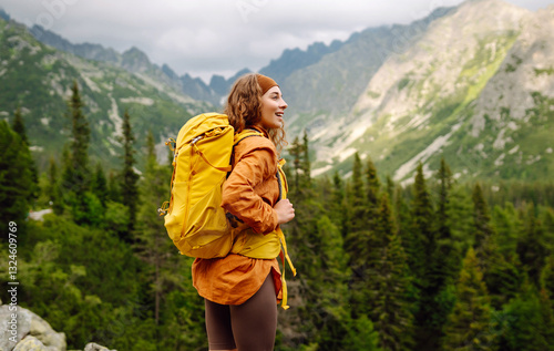 Obraz na płótnie An active female traveler with a bright hiking backpack enjoys the mountain view from the cliff. Young woman feels freedom on a hike. Adventure concept. w salonie