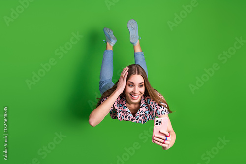Happy and stylish young woman with a casual yet trendy look taking a selfie in front of a vibrant green background expressing joy and charm