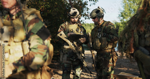 The military prepares for a field exercise as soldiers in camouflage uniforms with rifles and helmets review action details on a tablet and communicate with the army base.