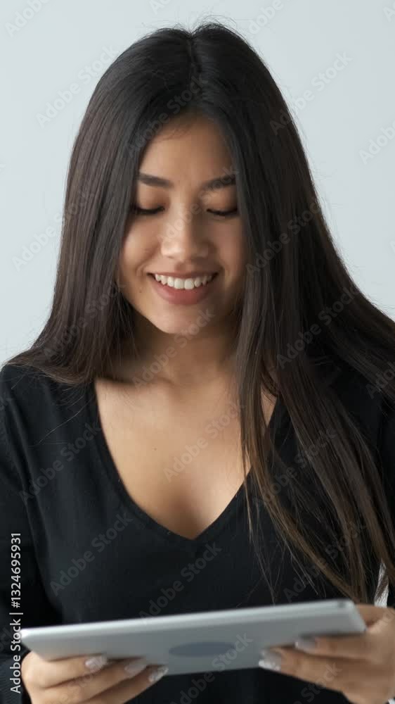 Asian woman playing video game on tablet PC, visibly upset after losing on a white background, emphasizing feelings of defeat and frustration during gaming. Vertical video. Asian woman playing video game on tablet PC, visibly upset after losing on a white background, emphasizing feelings of defeat and frustration during gaming. Vertical video.
