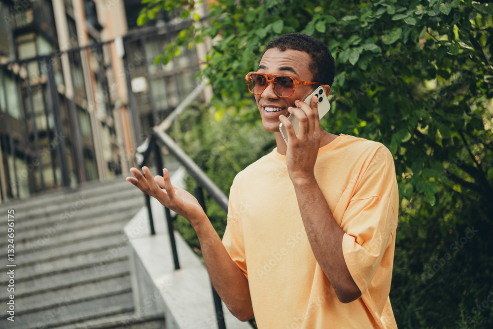 Obraz premium Young man enjoying a phone conversation while taking a stroll in the city on a sunny day with trendy sunglasses and a casual outfit