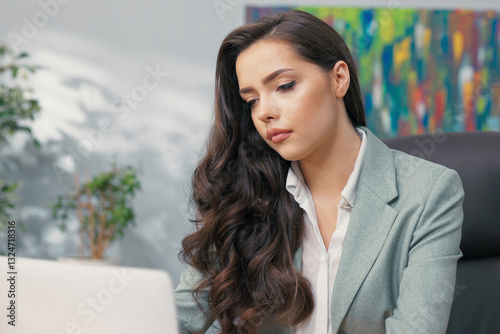 Elegant beautiful boss manager accounting worker secretary in office sits in front of laptop in company finishes work closes computer looks into camera with smile blanching on face with nice lips