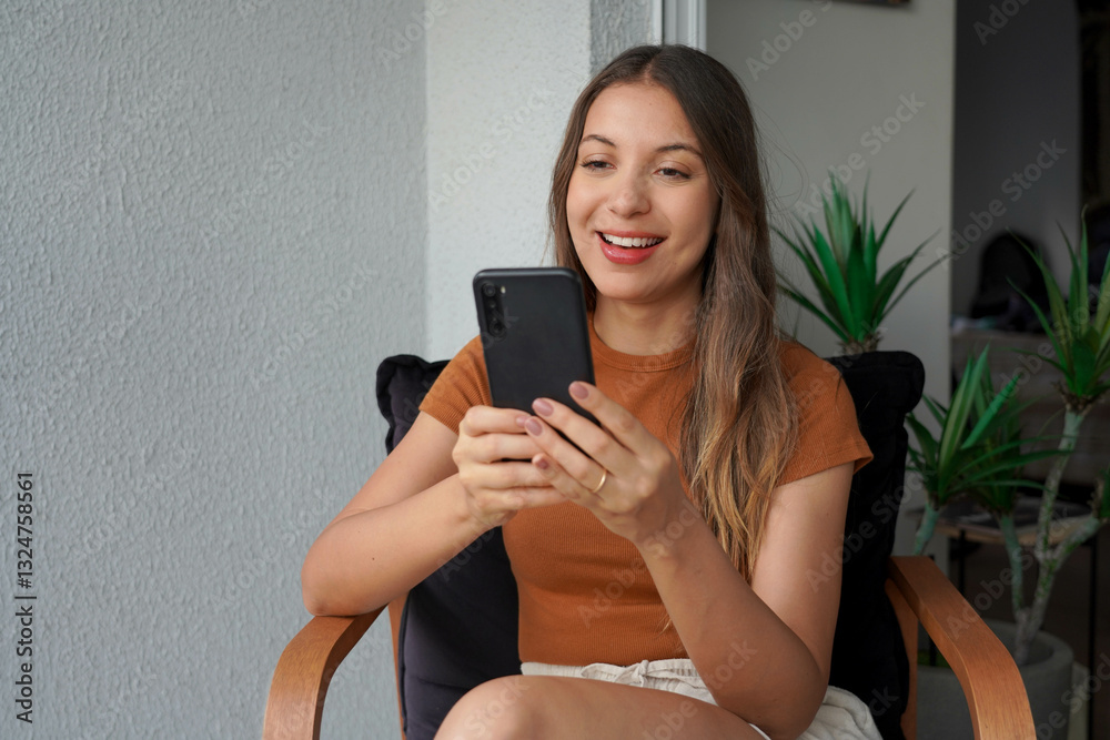 Hispanic young woman using smartphone app for chat on her apartment balcony Hispanic young woman using smartphone app for chat on her apartment balcony