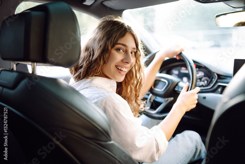Happy woman driving a car, enjoying a ride on a sunny day. Young female driver behind the wheel of a car sharing. Transport, travel concept. Lifestyle.