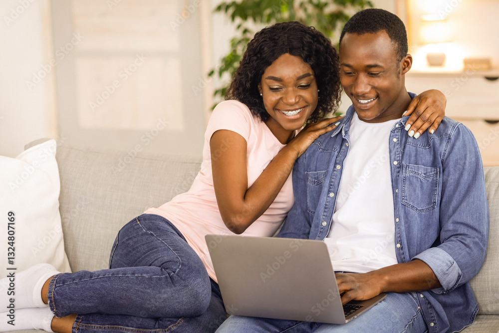 Cheerful black couple using laptop while resting on couch at living room at home, watching funny content together, copy space. African american loving family husband and wife spending time together Cheerful black couple using laptop while resting on couch at living room at home, watching funny content together, copy space. African american loving family husband and wife spending time together
