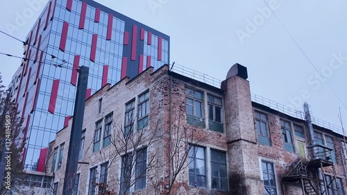 An old abandoned factory with damaged walls on the background of modern structures in the same area