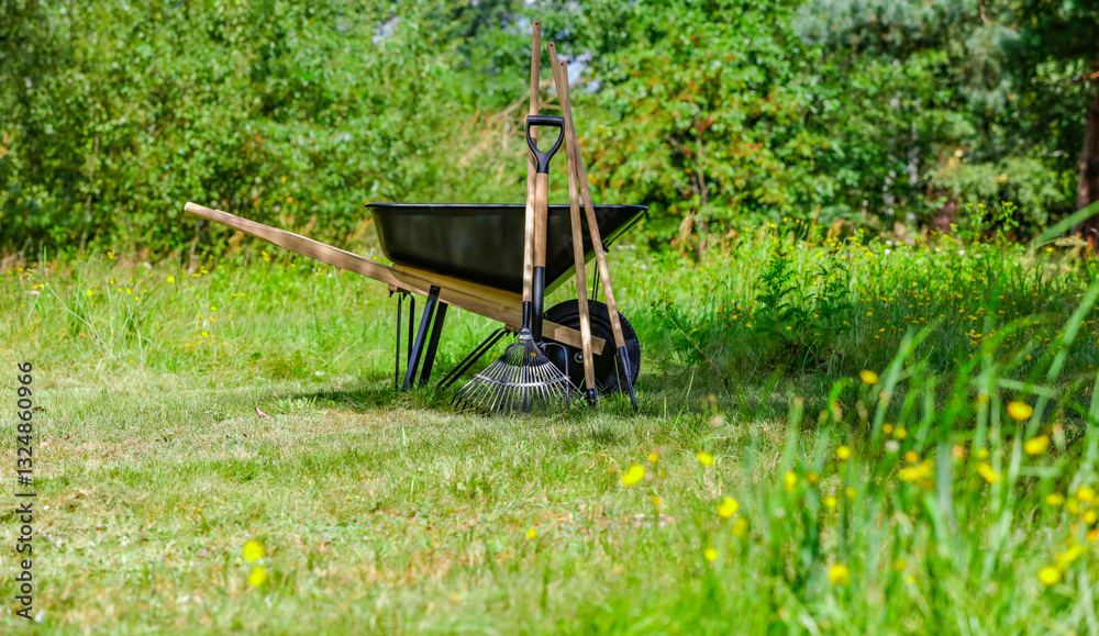 Garden tools and wheelbarrow on grassy lawn with green background of garden or park setting. Outdoor work and gardening. Garden tools and wheelbarrow on grassy lawn with green background of garden or park setting. Outdoor work and gardening.